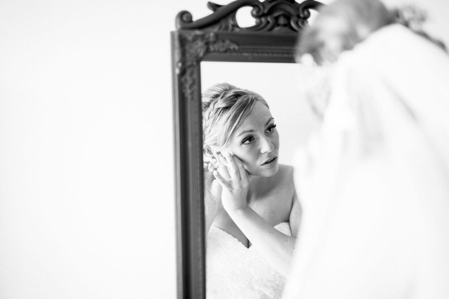 Die Braut sieht in den Spiegel und steckt sich ihre Ohrringe an.
