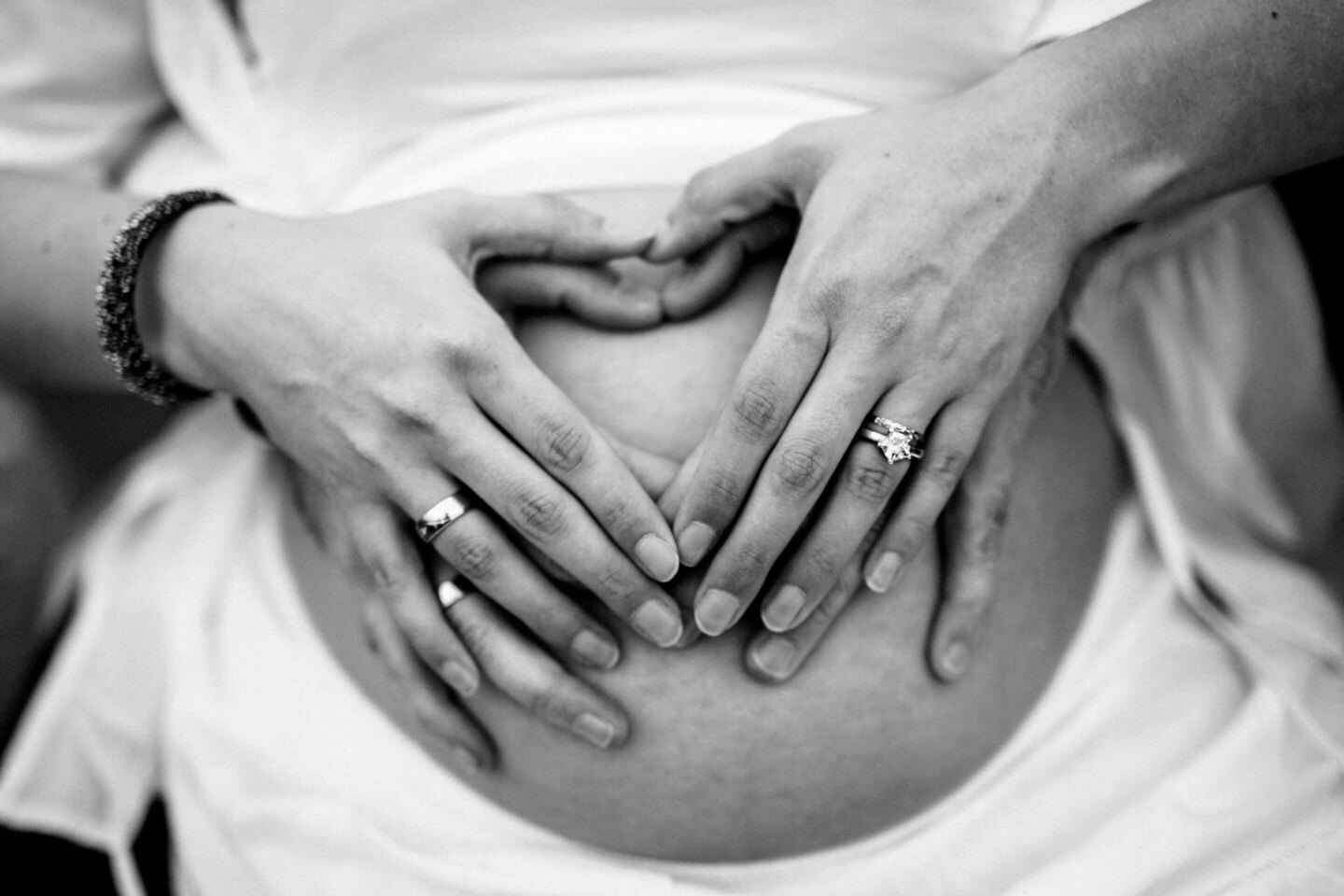 vier Hände bilden ein Herz auf dem schwangeren Bauch beim Baby Belly Shooting