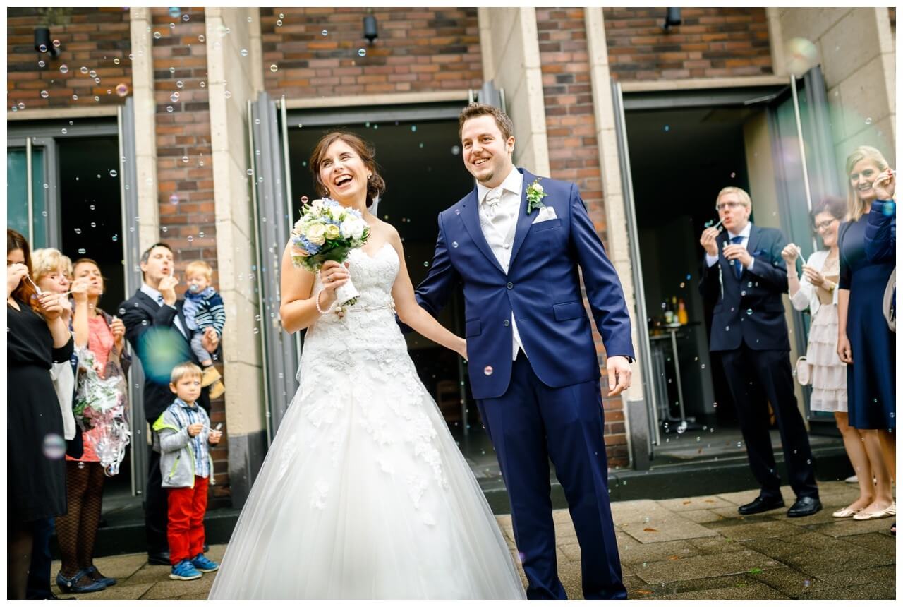 Das Brautpaar steht vor der Kirche und wird lachend von den Gästen vor der Kirche in Gelsenkirchen empfangen.