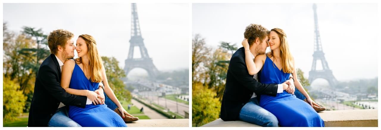 Engagementshooting in Paris, das Paar sitzt auf einer Mauer vor dem Eiffelturm und kuschelt.
