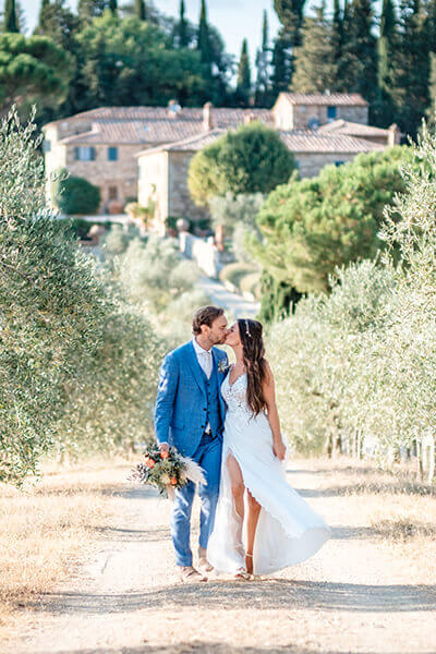 Hochzeitsreportage, Brautpaar küsst sich bei freier Trauung auf einem Zypressenweg zwischen Olivenbäumen in Italien